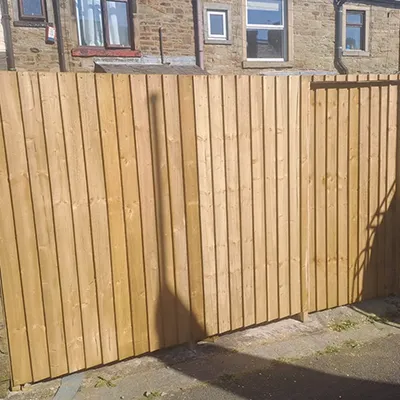 A man riding a skateboard next to a tall wooden fence.
